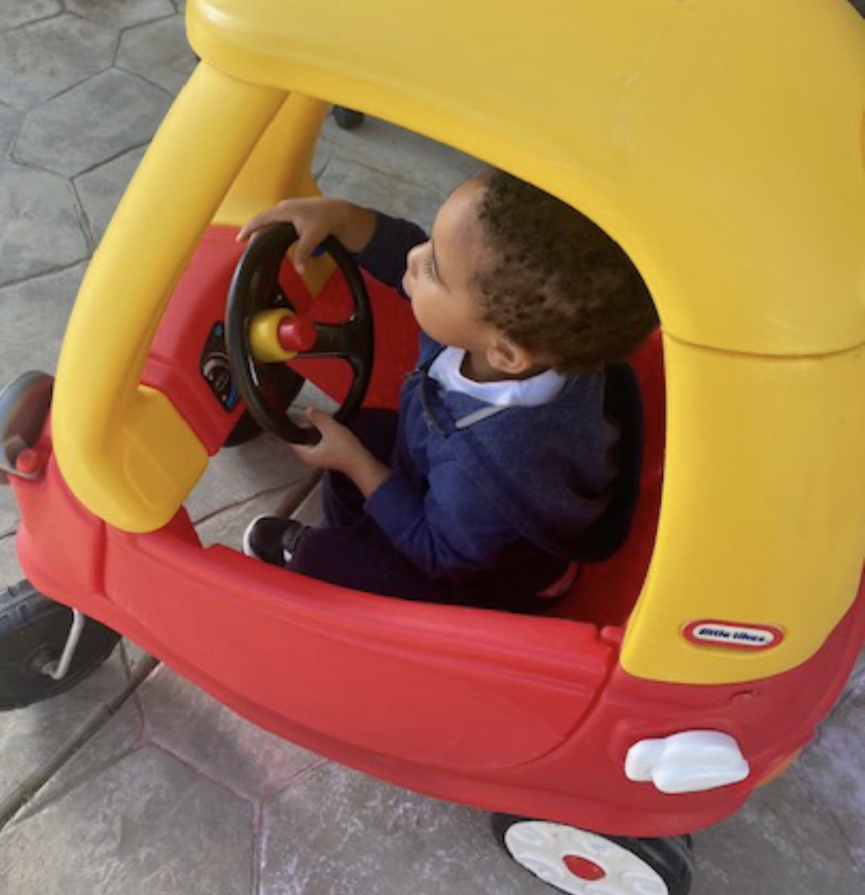 Toddler steering a red and yellow cozy coupe car