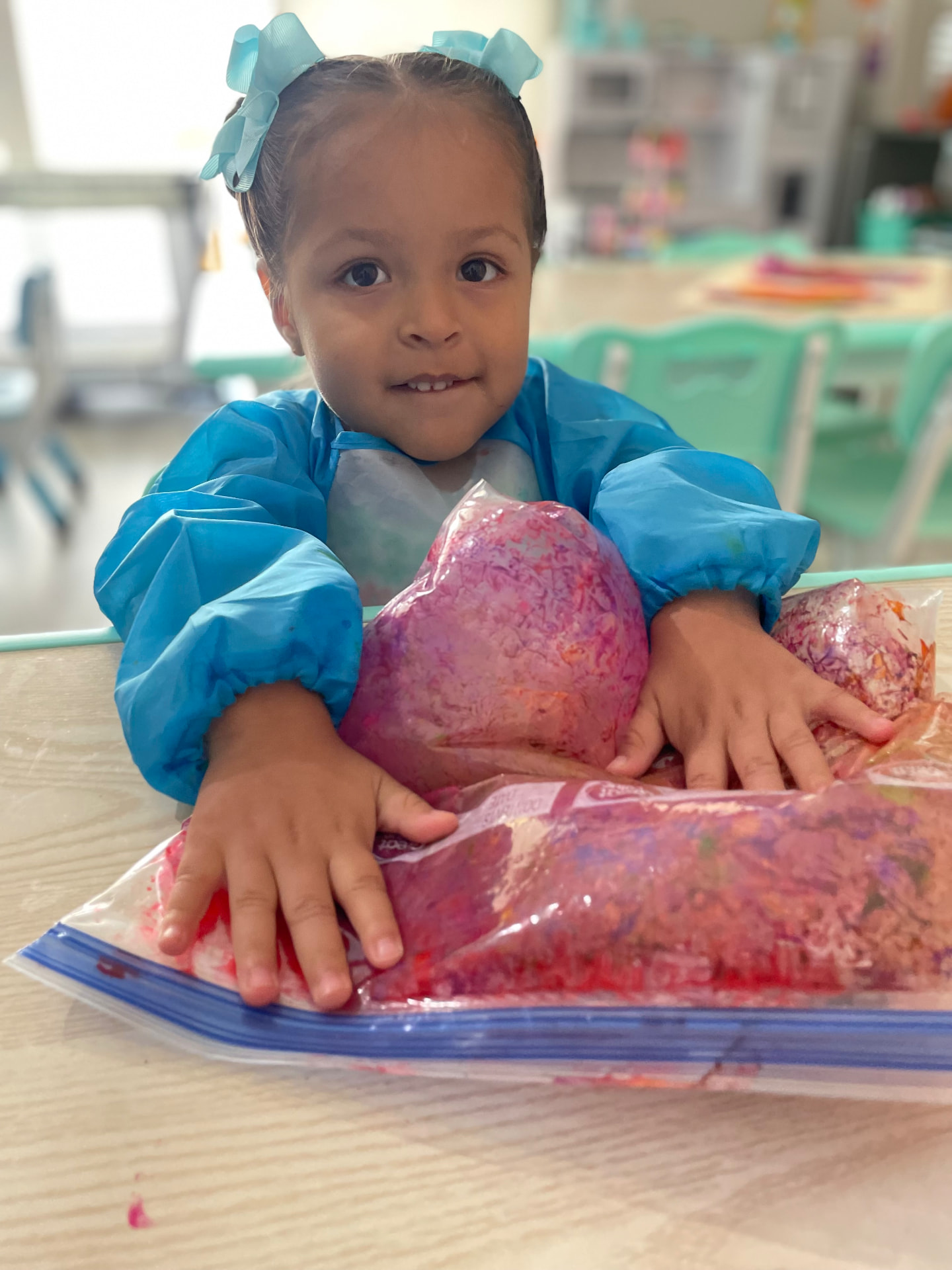 Child in a smock squishing colorful sensory paint bags