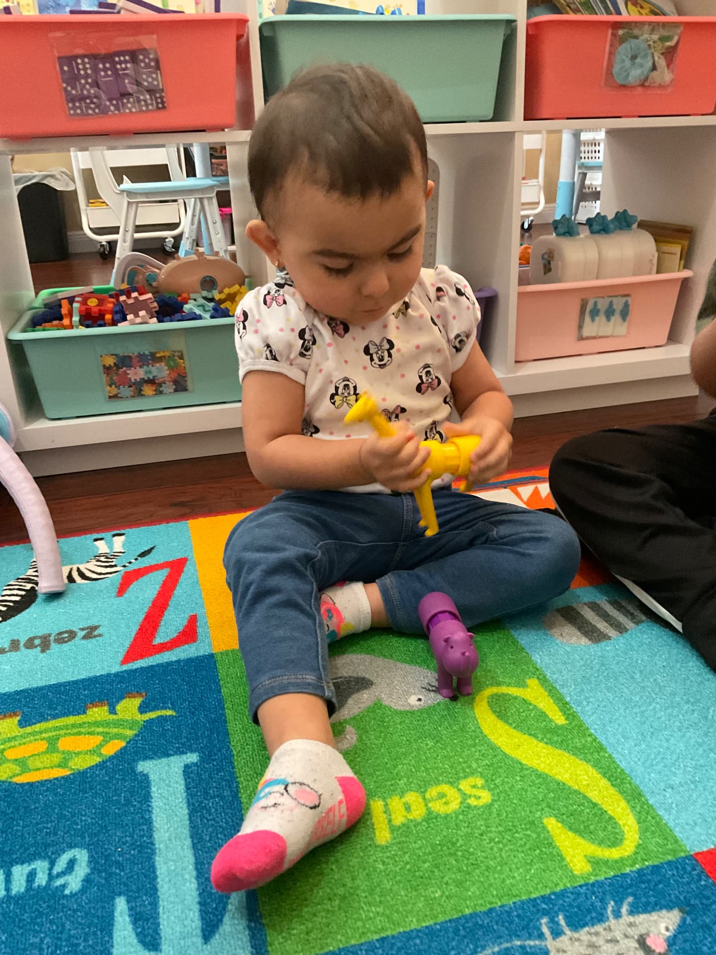 Toddler playing with animal figures on an alphabet rug