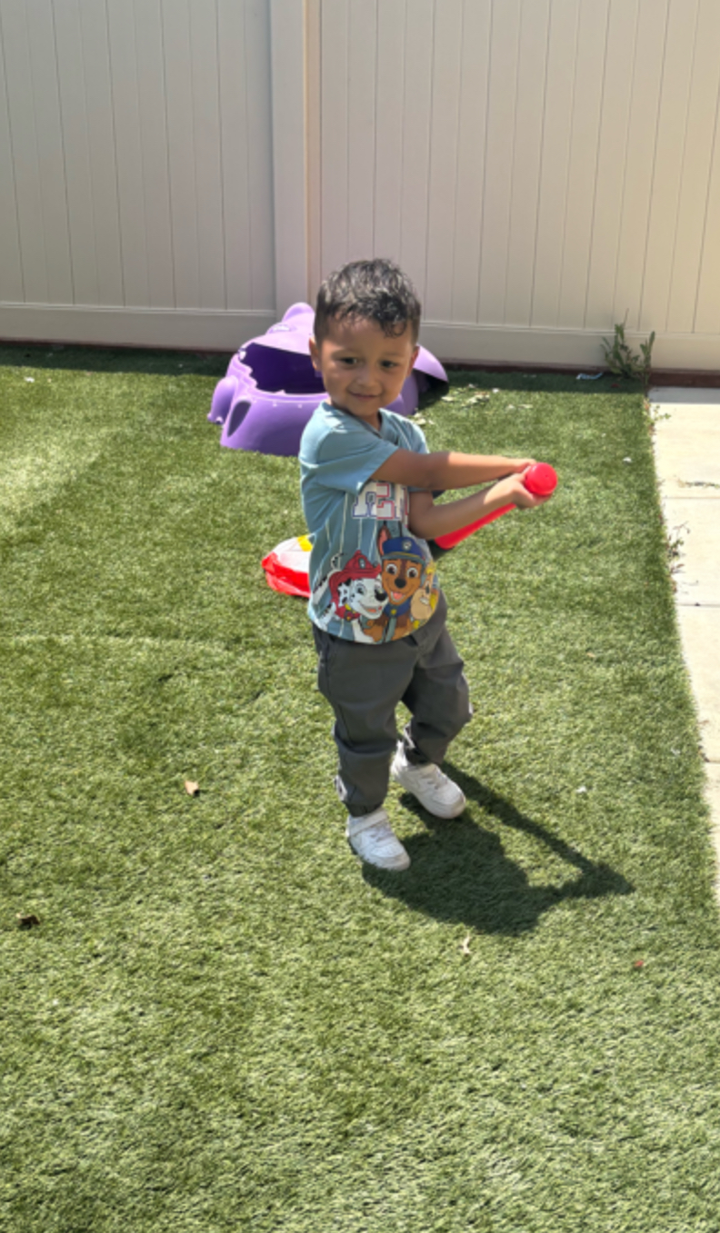 Preschooler swinging a red bat on the backyard turf