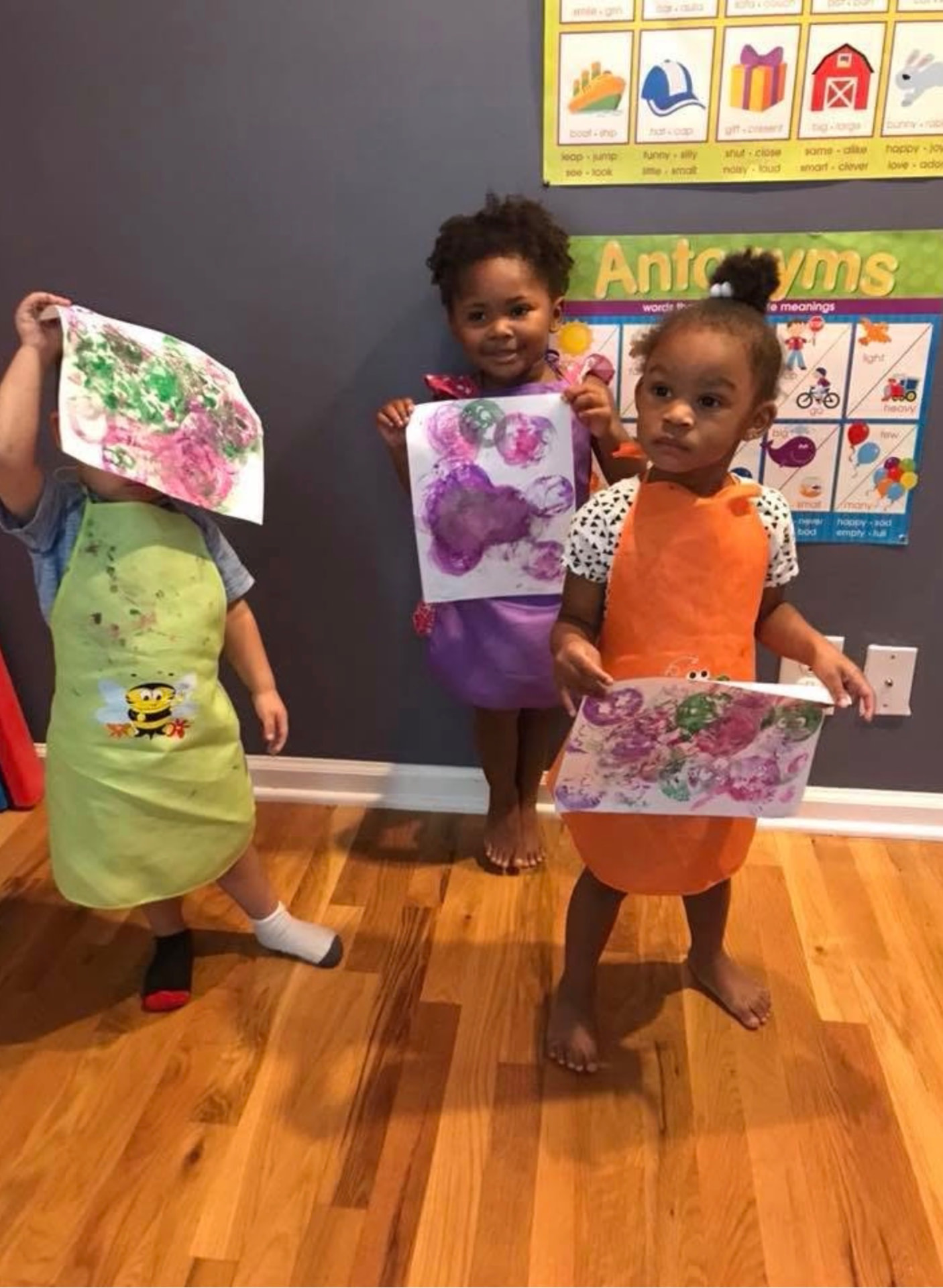 Three children in smocks holding up their painted artwork