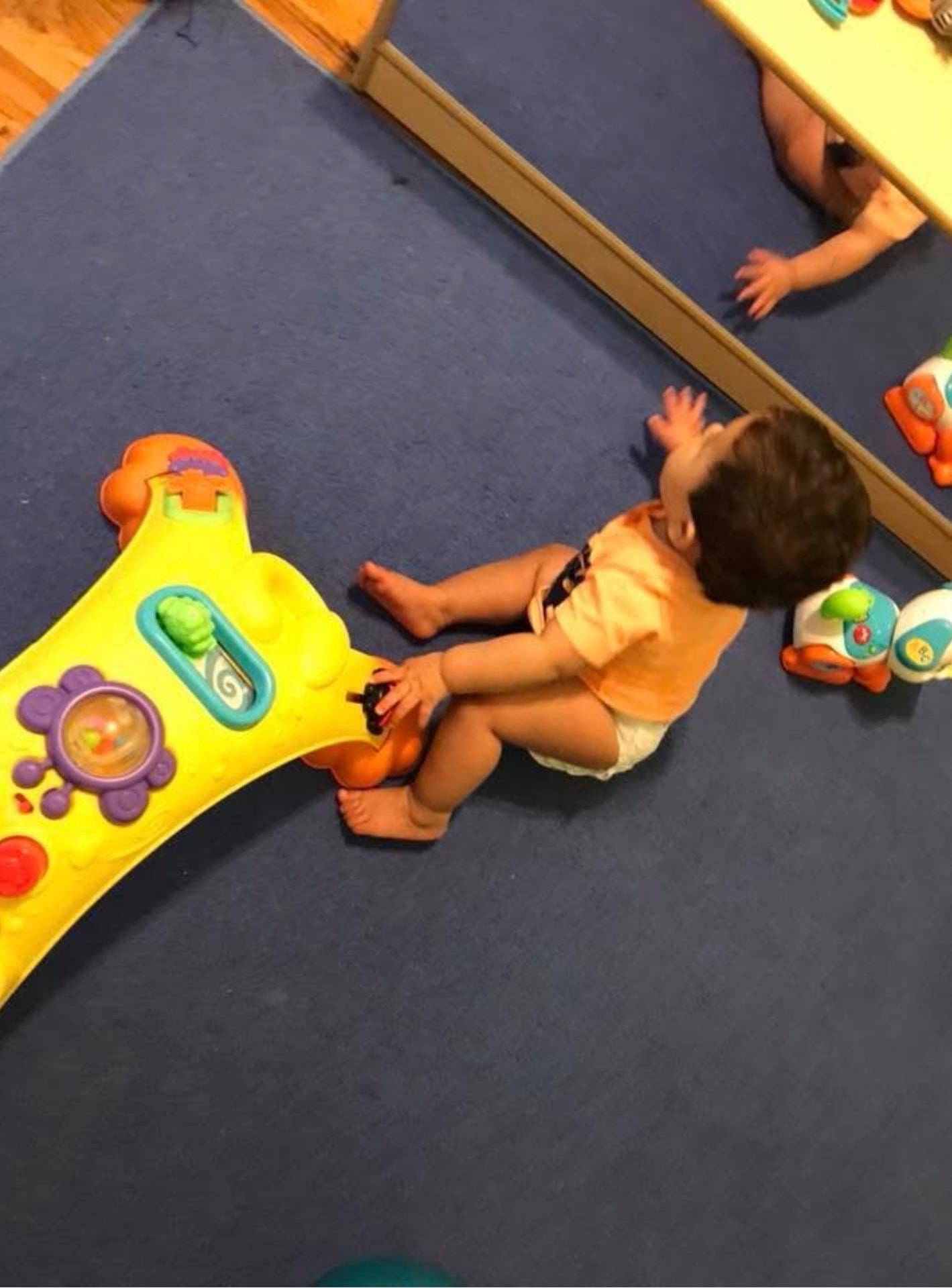 Infant playing by the floor mirror with activity toys