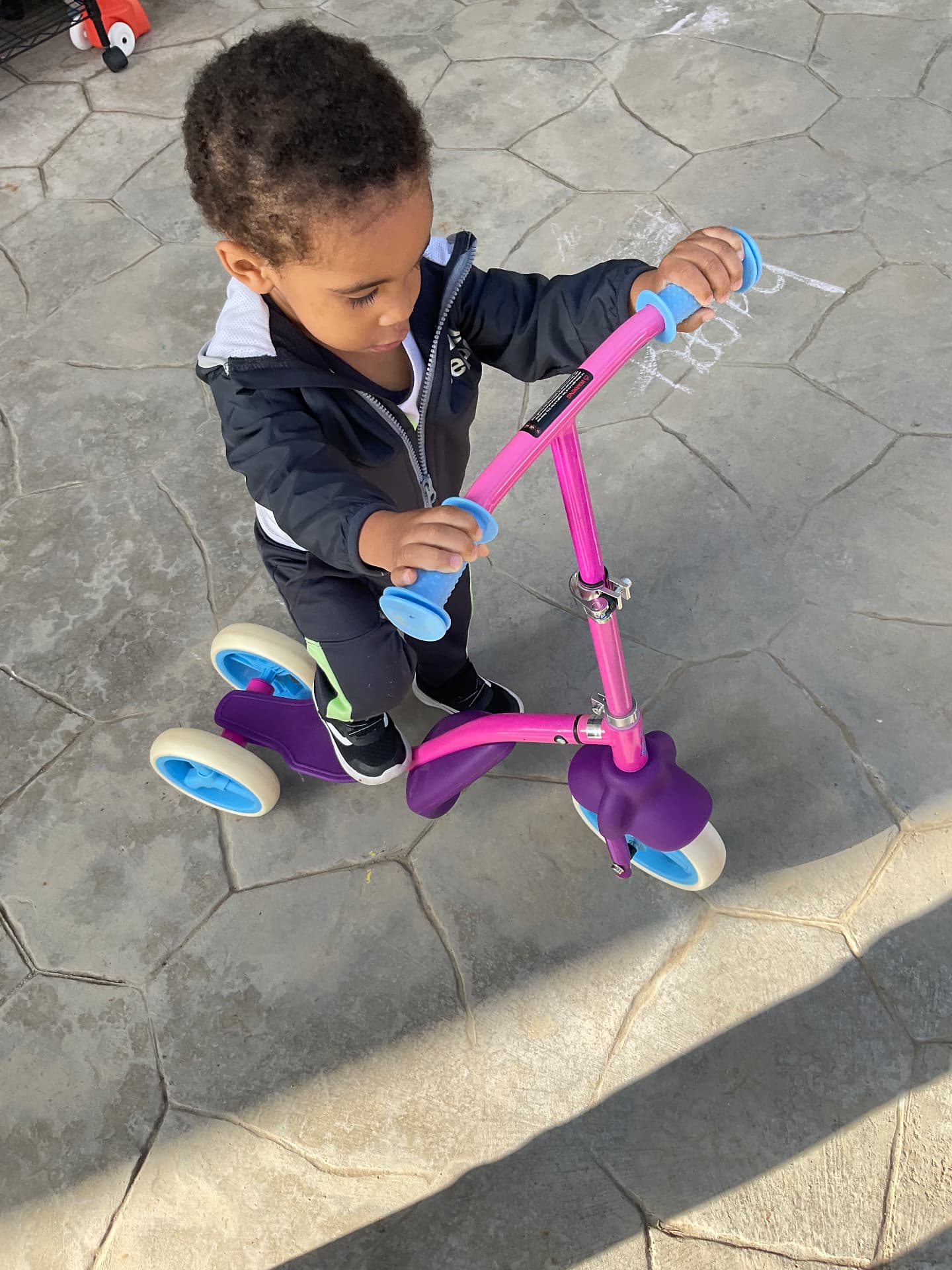 Toddler riding a pink and purple scooter on the patio