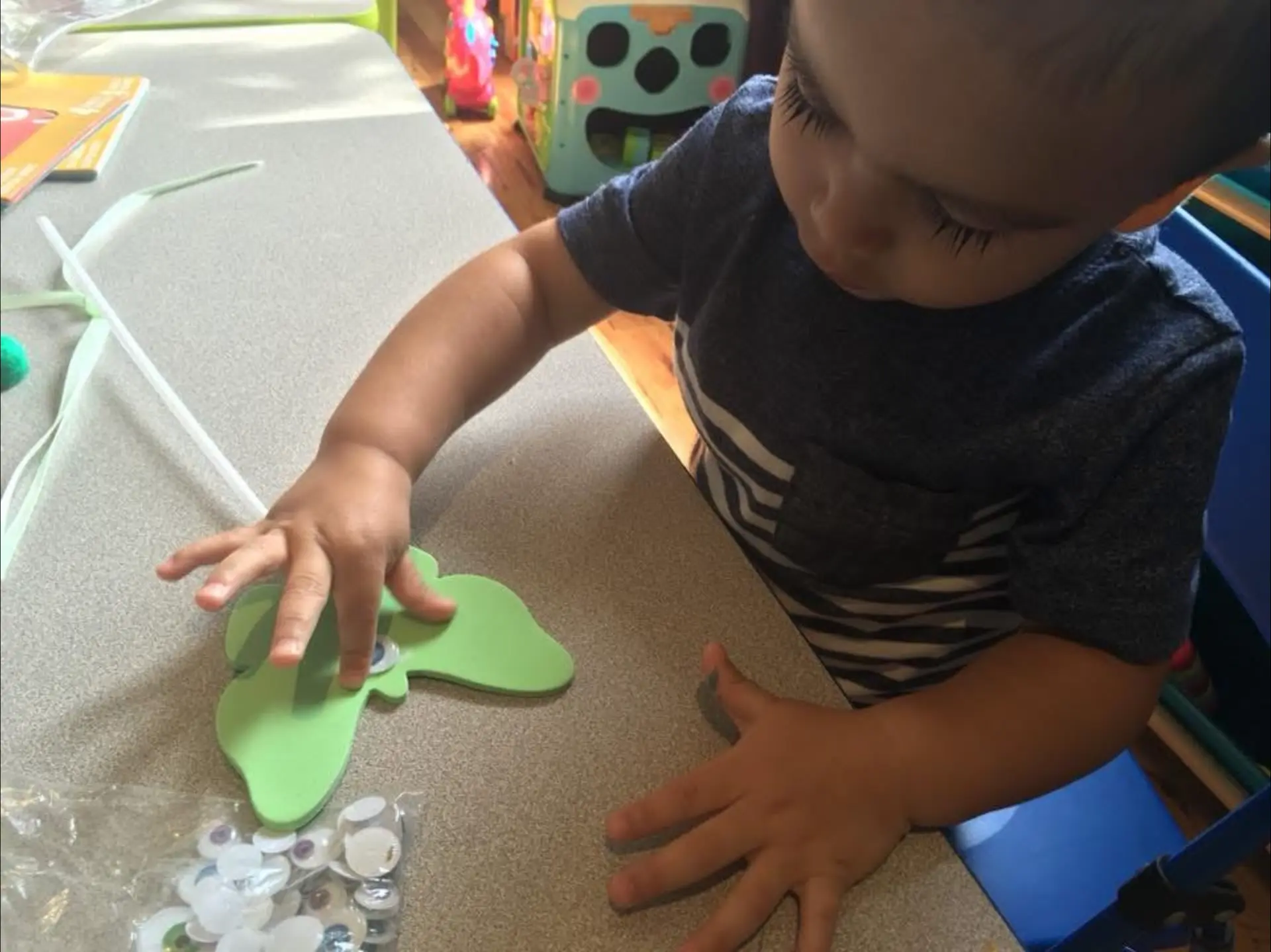 Child adding googly eyes to a green foam craft