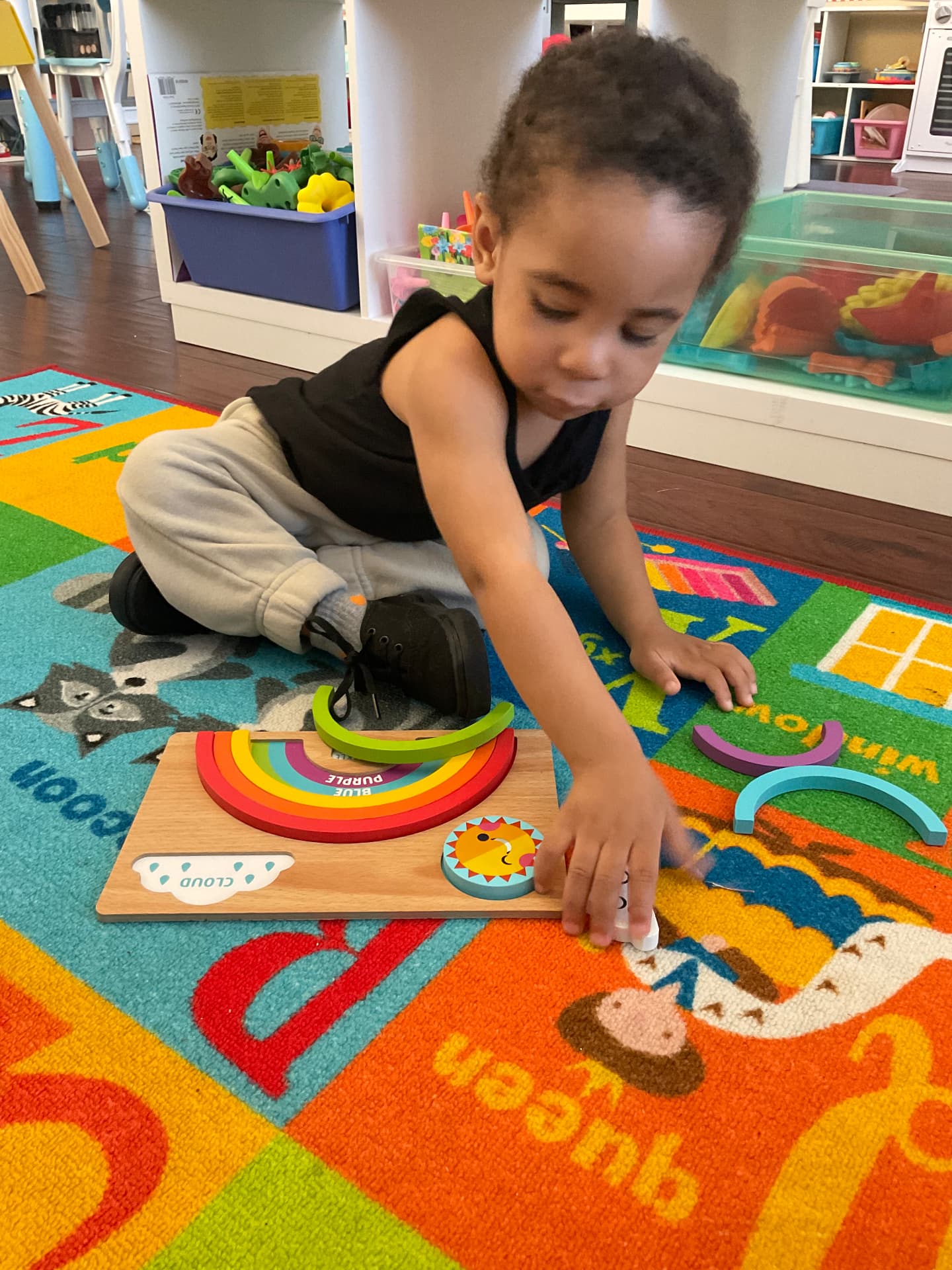 Toddler assembling a wooden rainbow color puzzle on the alphabet rug