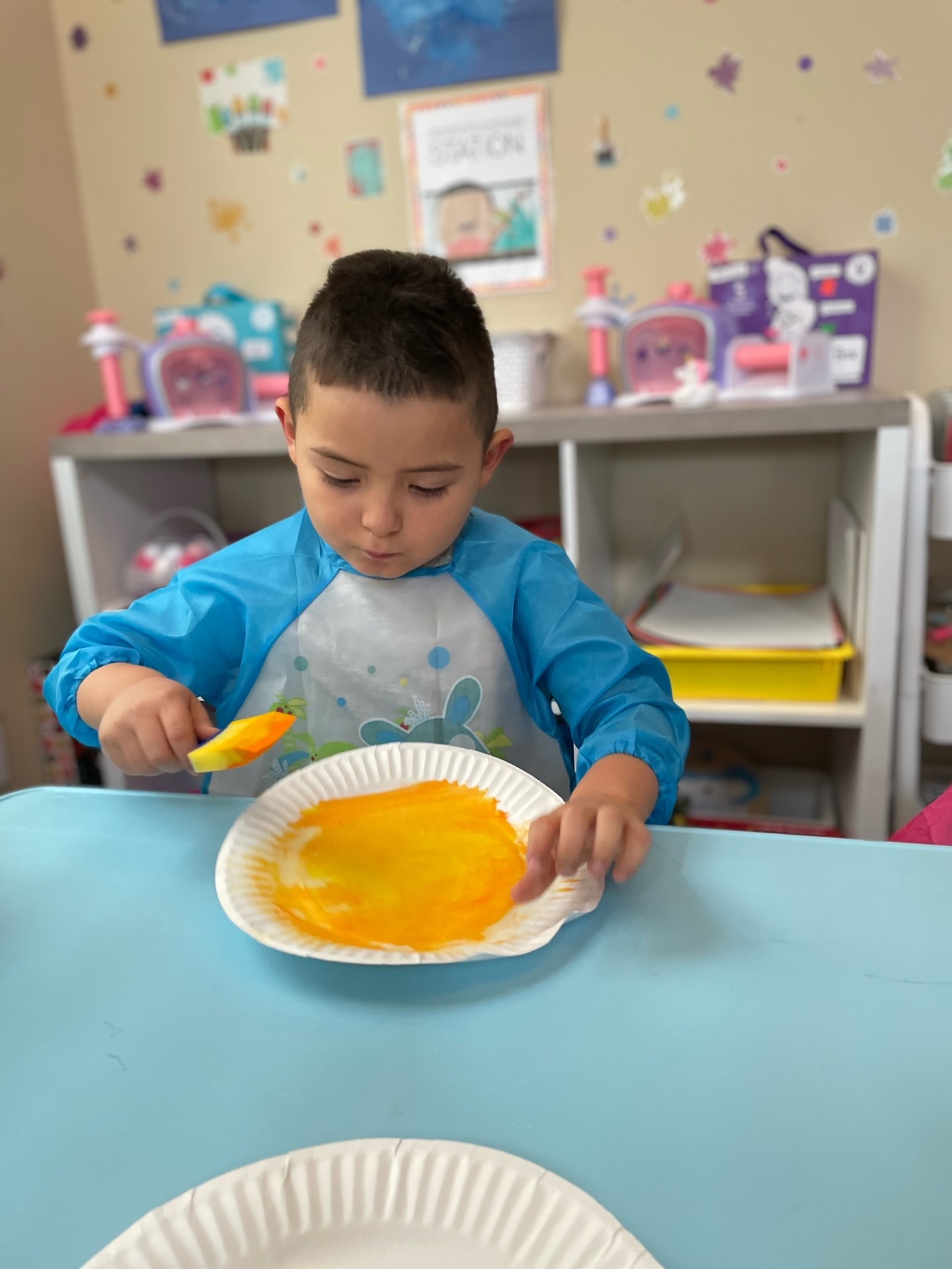 Preschooler in a smock painting a paper plate bright orange