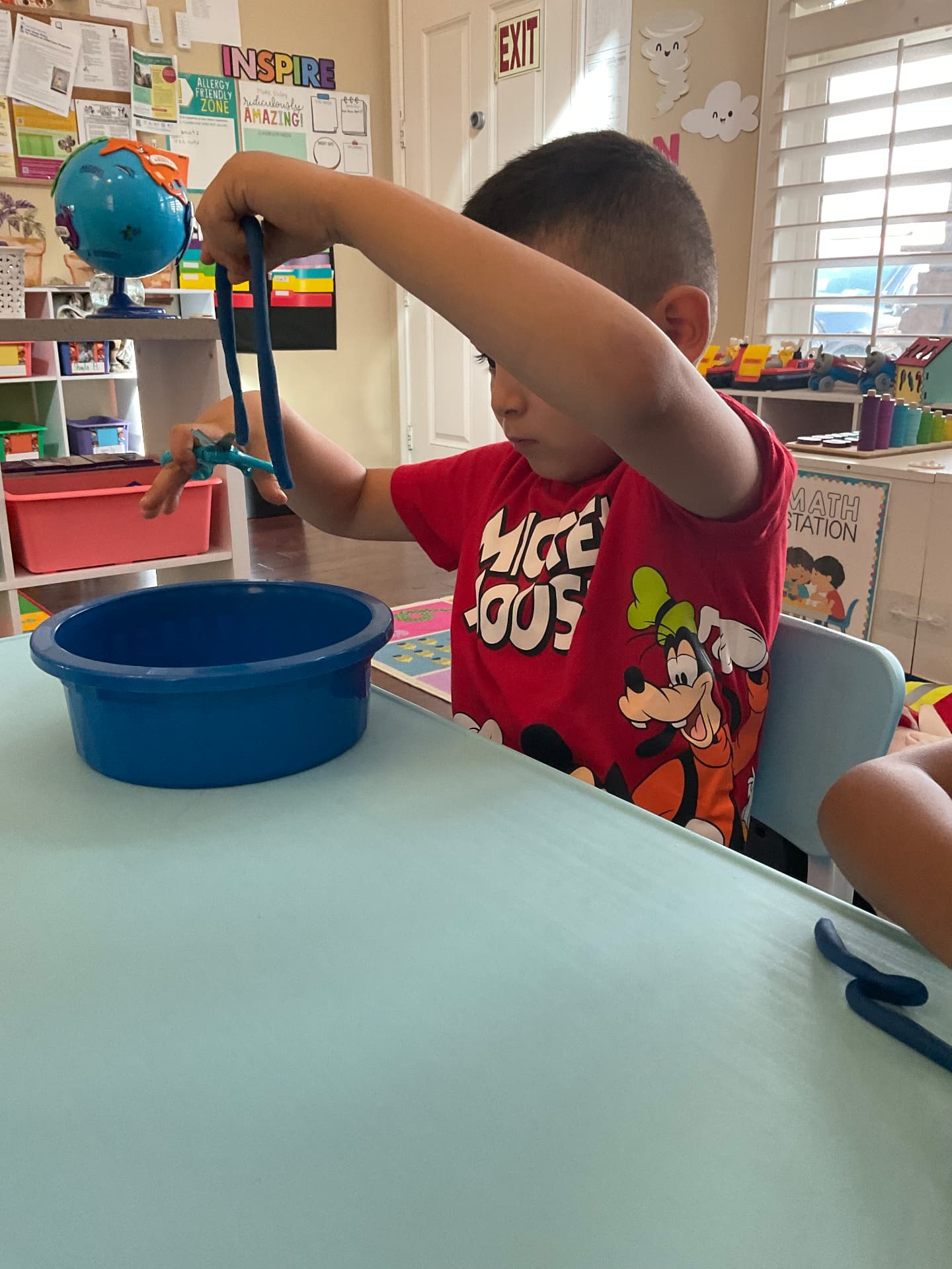 Child snipping a strand of play dough with scissors at the table