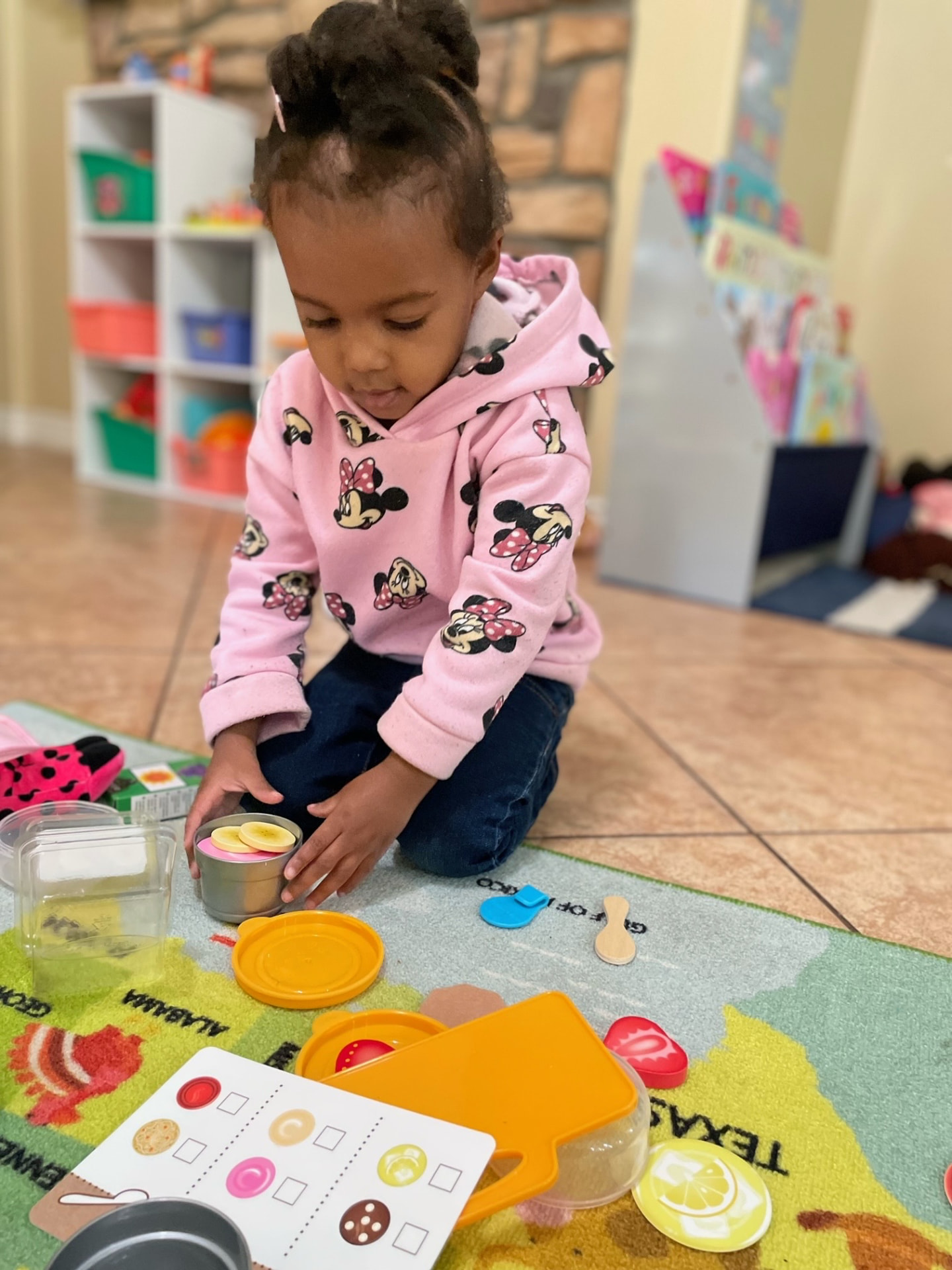 Toddler serving pretend banana slices in a toy pot on a USA map rug