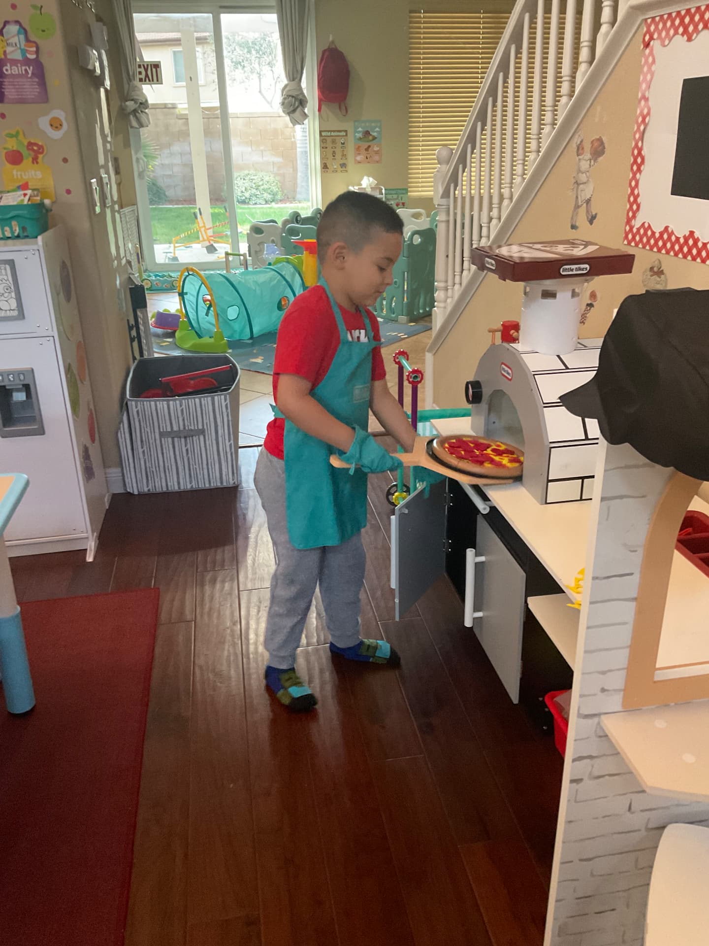 Child in an apron sliding a pretend pizza into the play oven