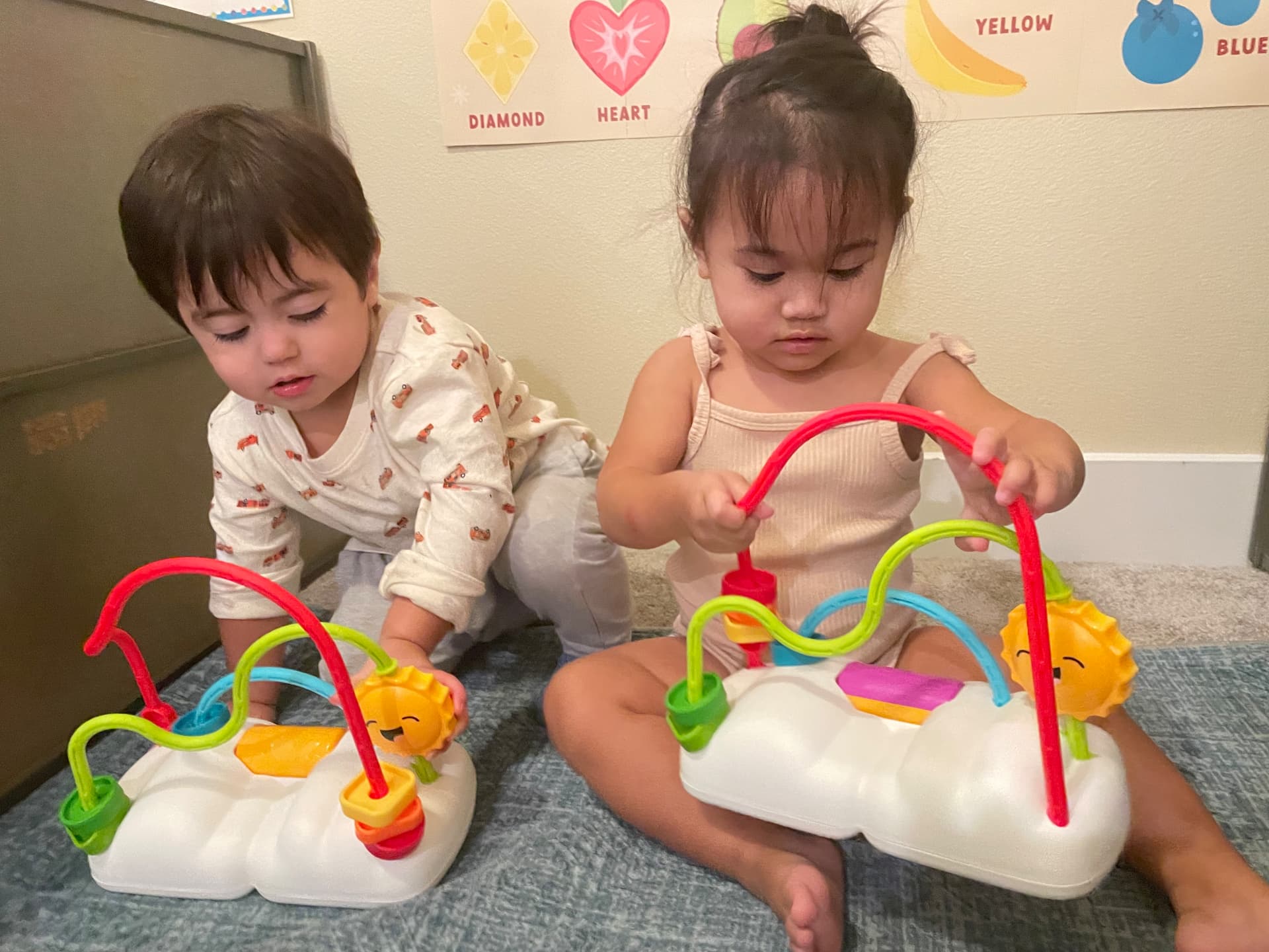 Two toddlers playing side by side with rainbow bead mazes