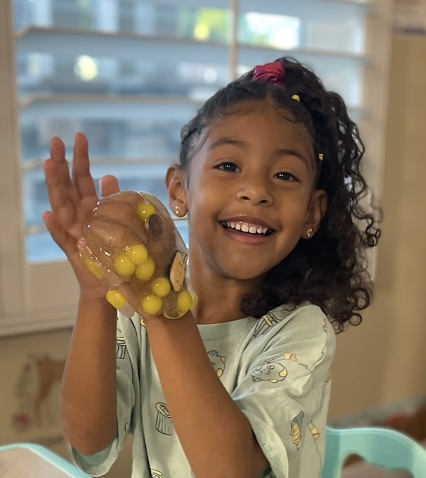 Child laughing while squishing slime filled with yellow beads