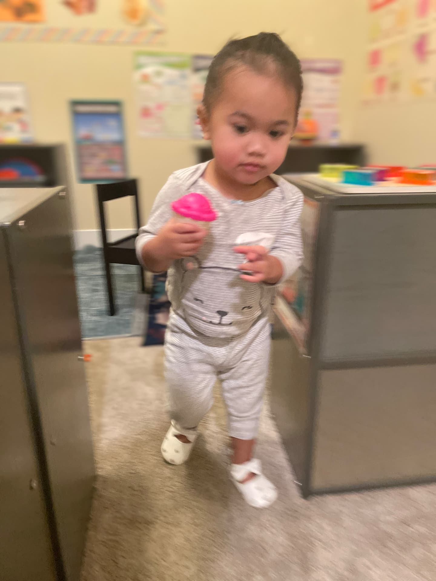 Toddler carrying a pretend ice cream cone across the playroom