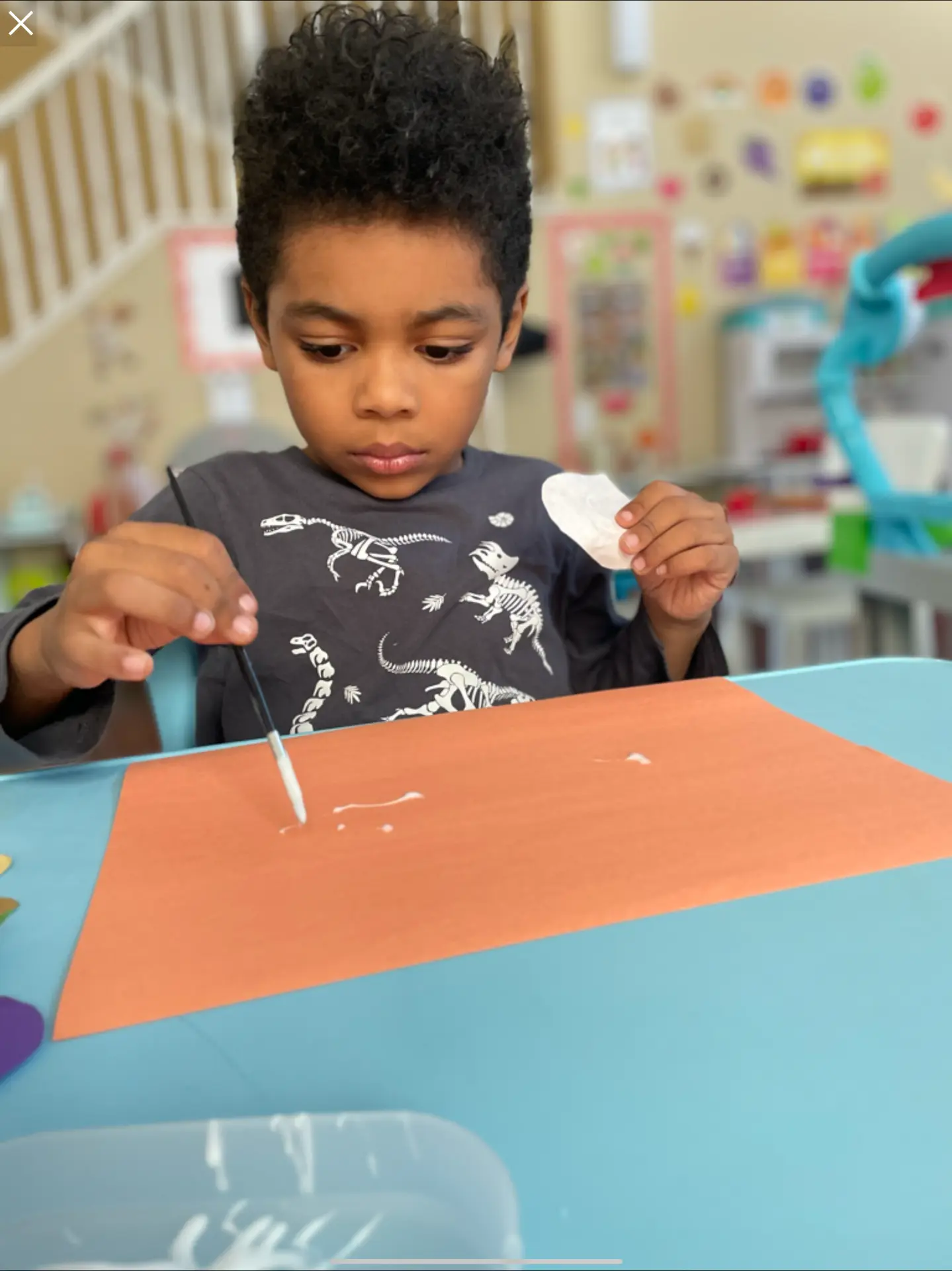 Preschooler brushing glue onto orange paper for a collage