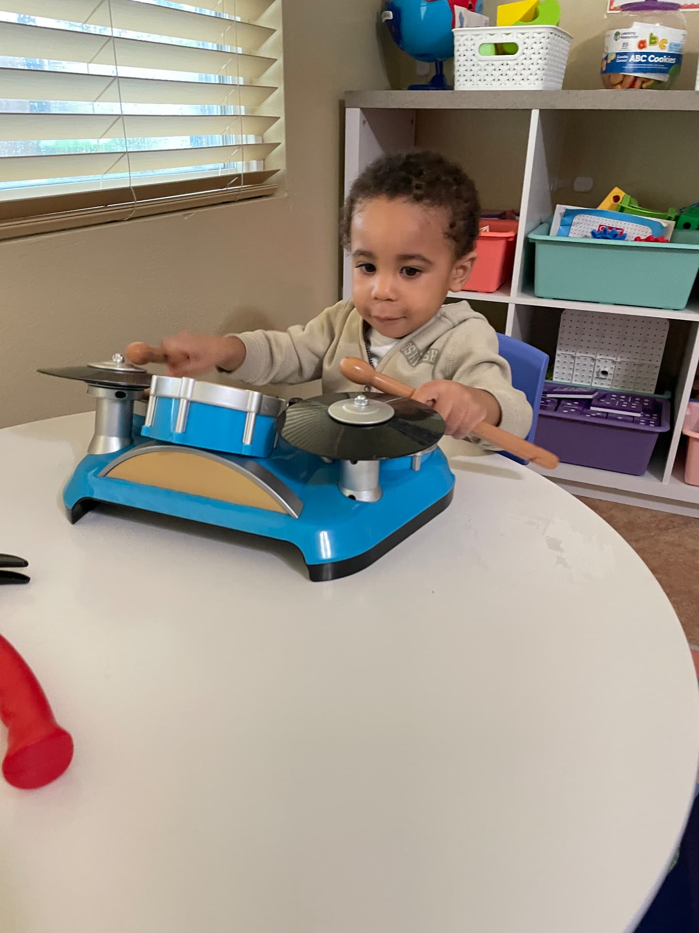 Toddler playing a toy drum set with wooden drumsticks
