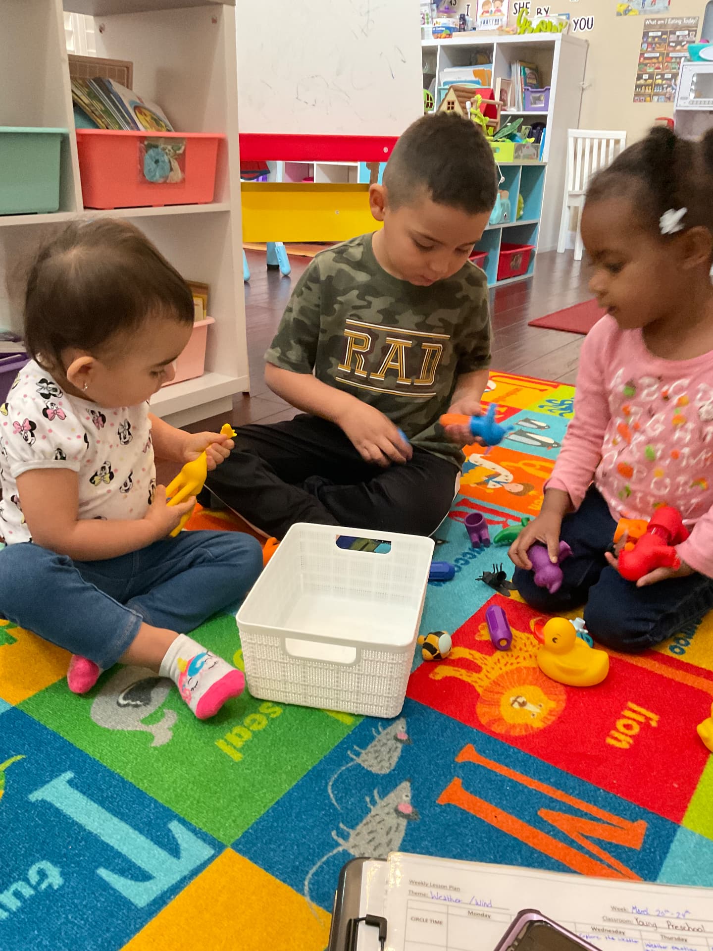 Three children sharing animal figures on a colorful alphabet rug