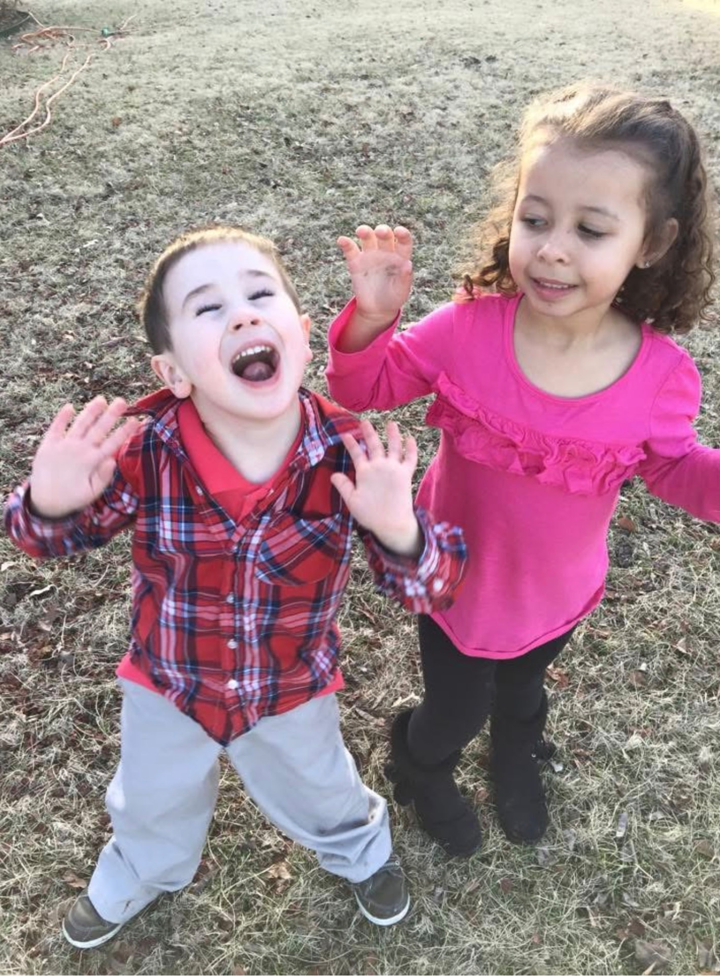 Two children being silly outside with hands in the air