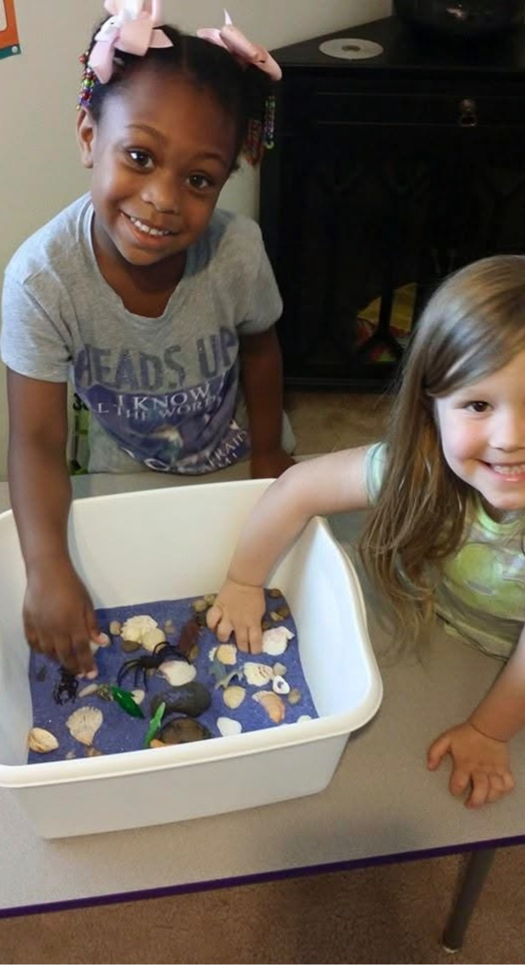Two children exploring a sensory bin with shells and sea creatures