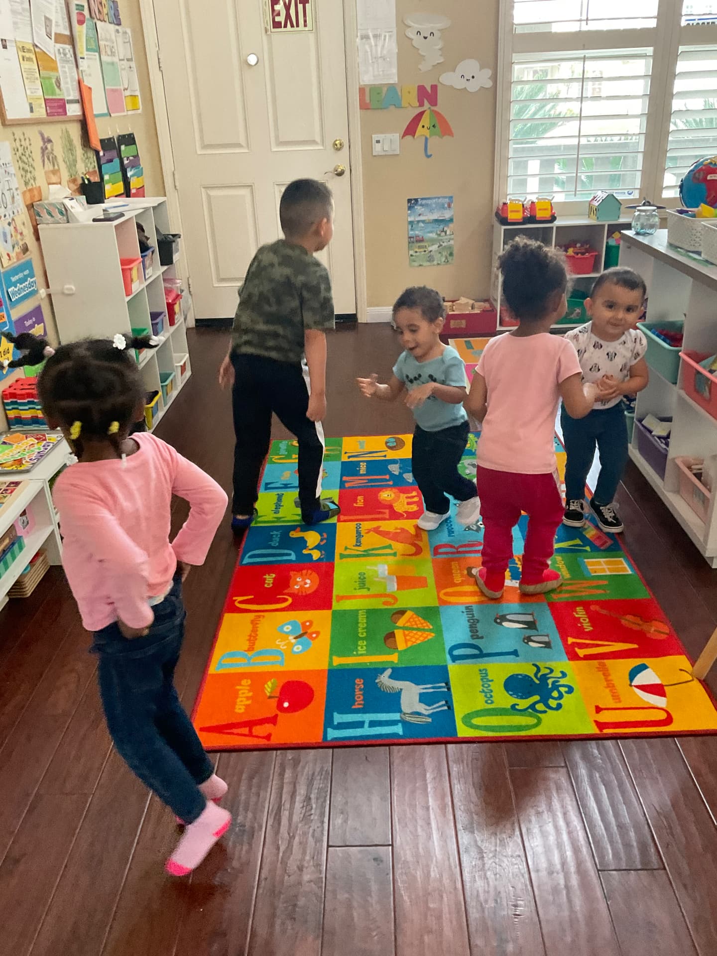 Five children dancing together on the alphabet rug