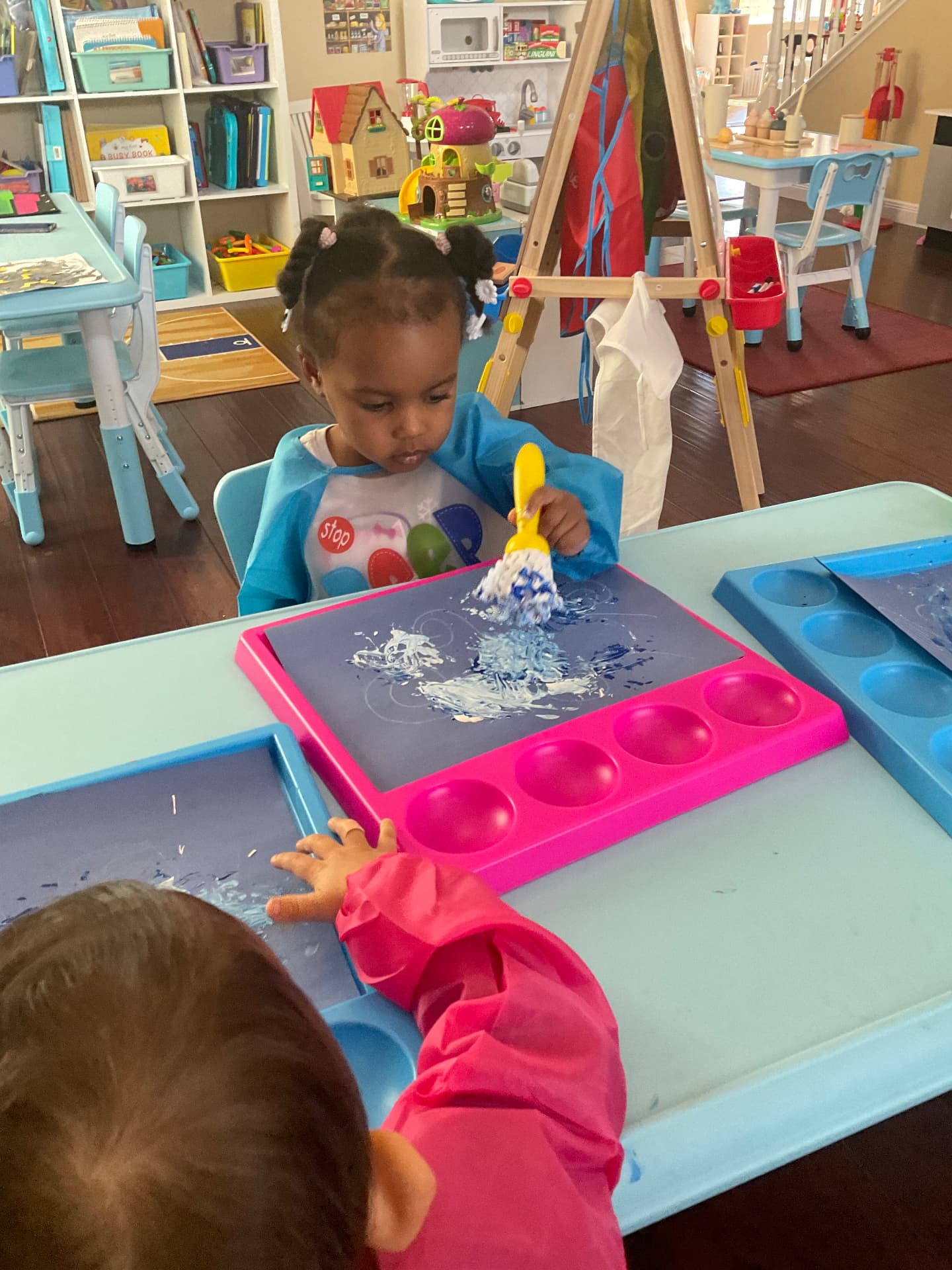 Two children brush painting with blue and white paint on trays