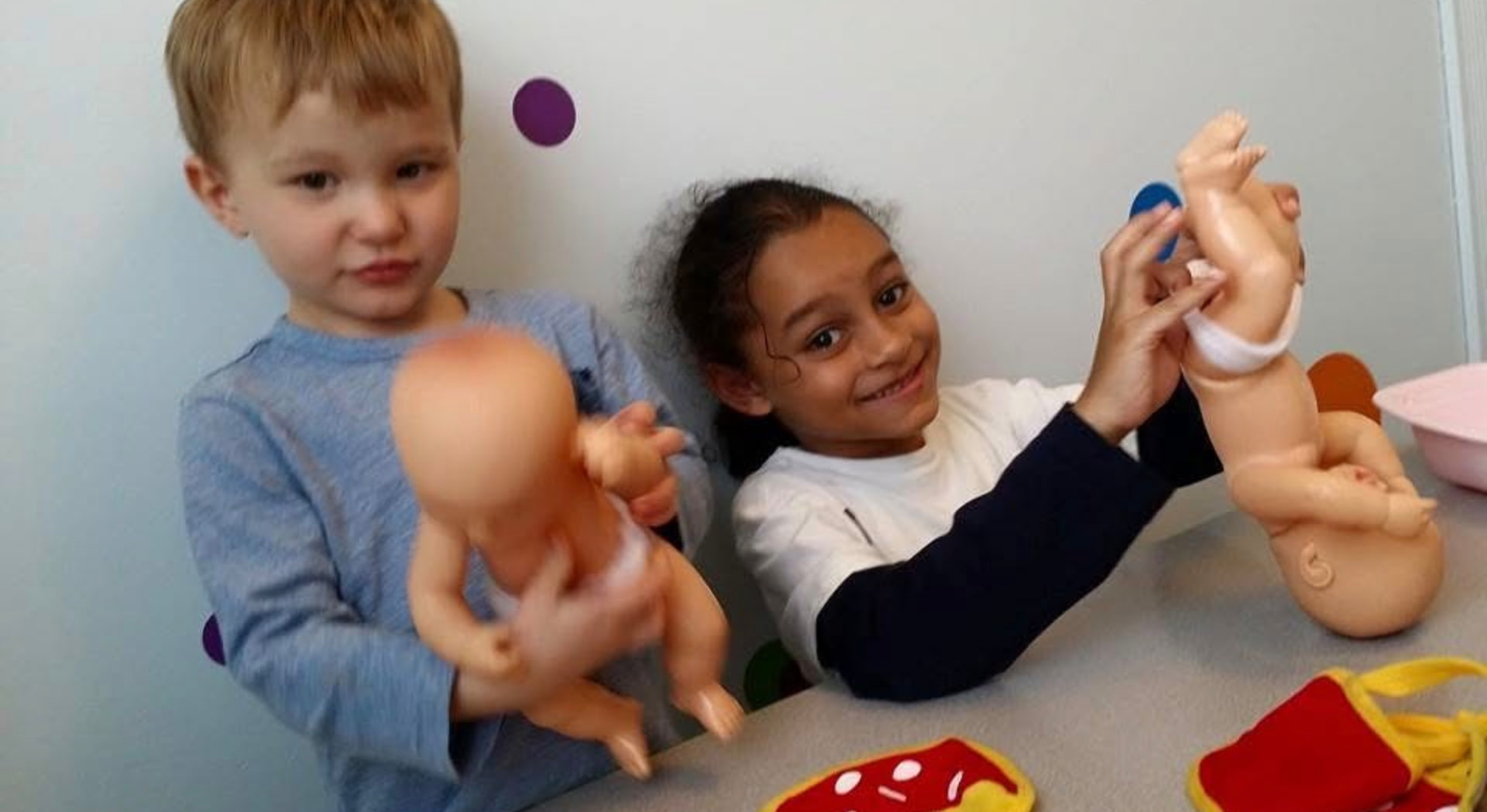 Two children smiling while holding baby dolls