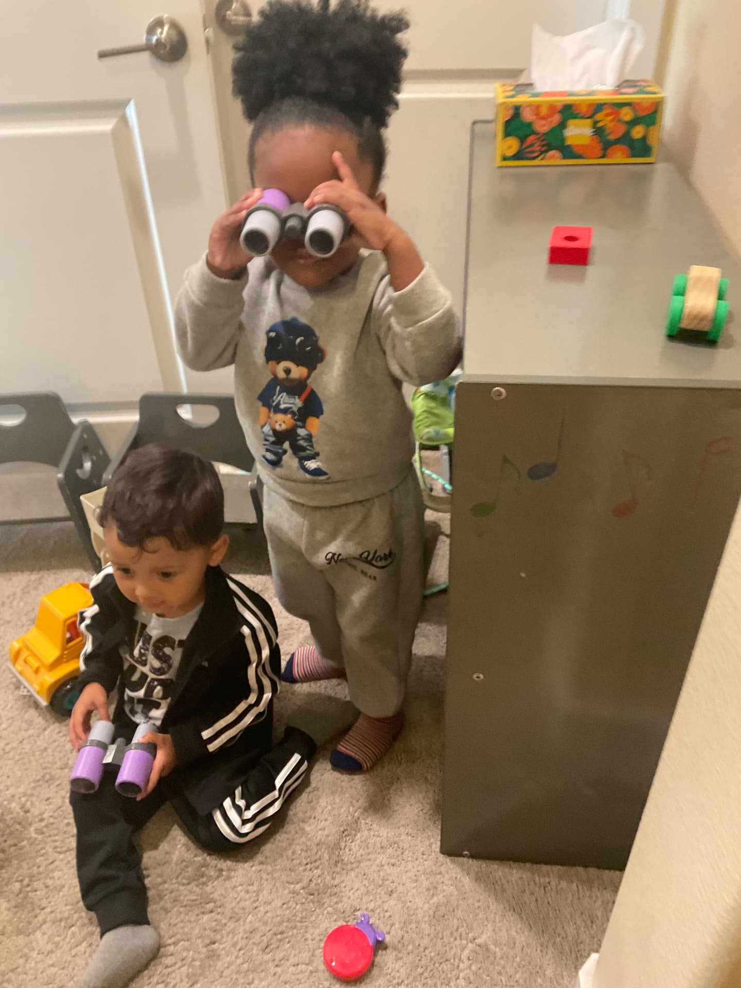 Two toddlers exploring the room with toy binoculars