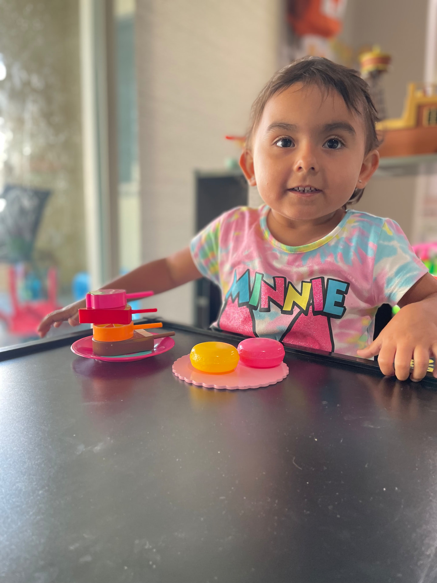 Toddler playing with pretend desserts at a play kitchen table