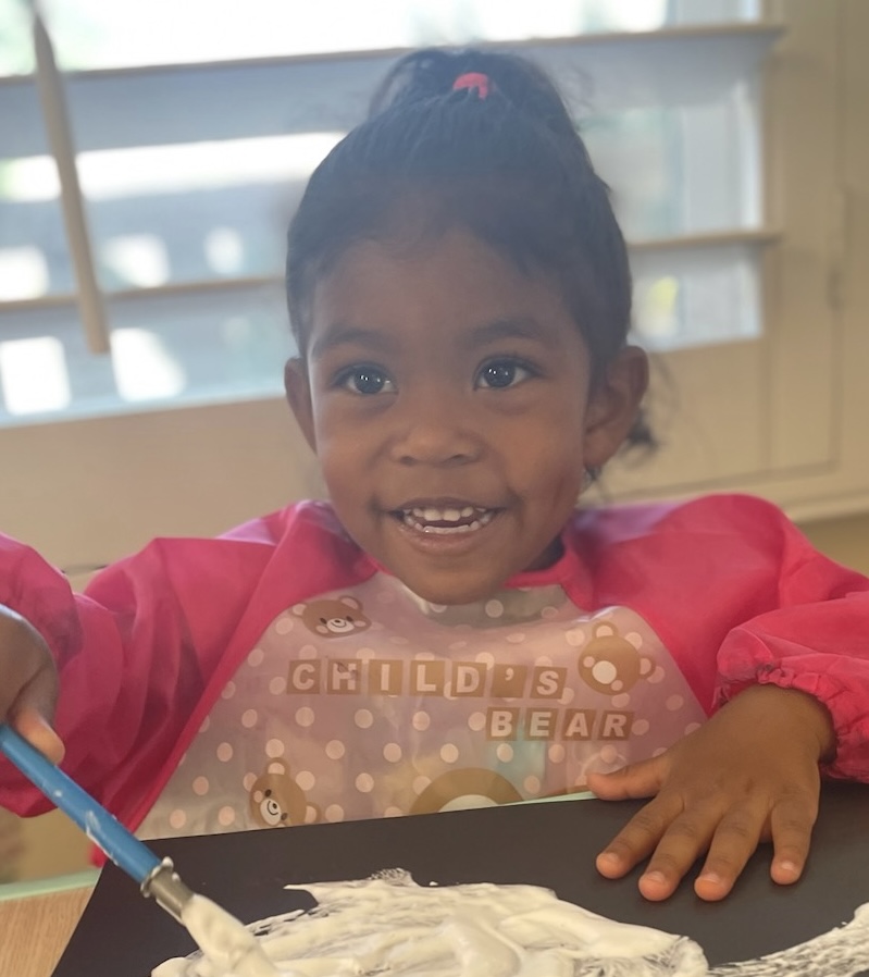 Smiling child in a smock spreading shaving cream on a black tray