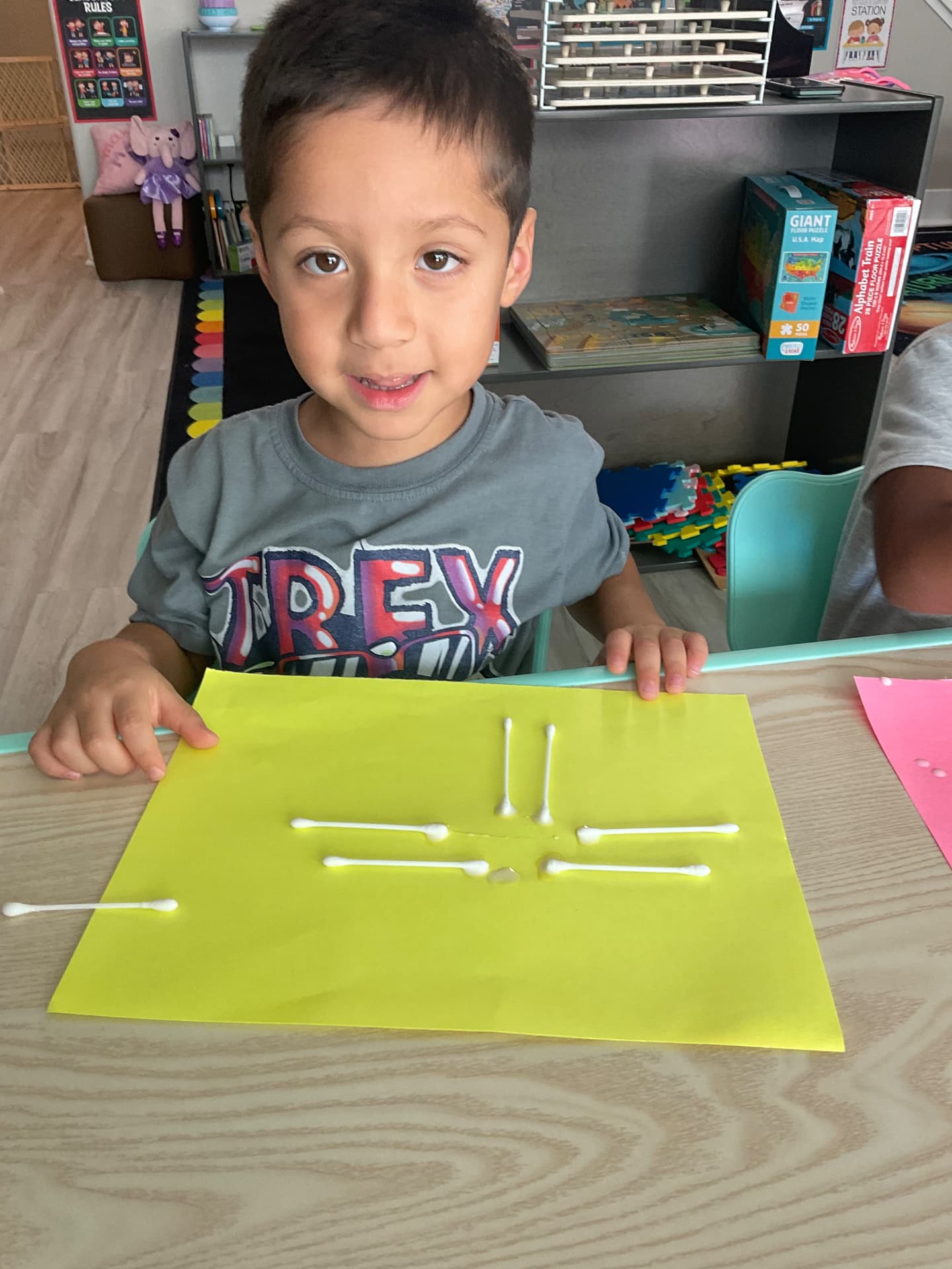 Preschooler showing a cotton swab collage on yellow paper