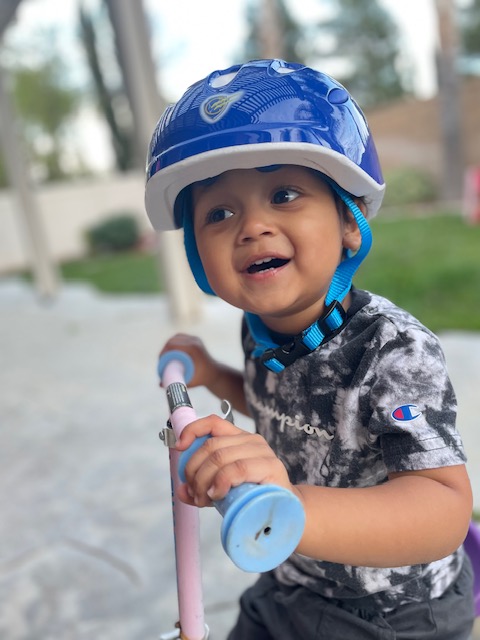 Smiling child in a helmet riding a scooter outside