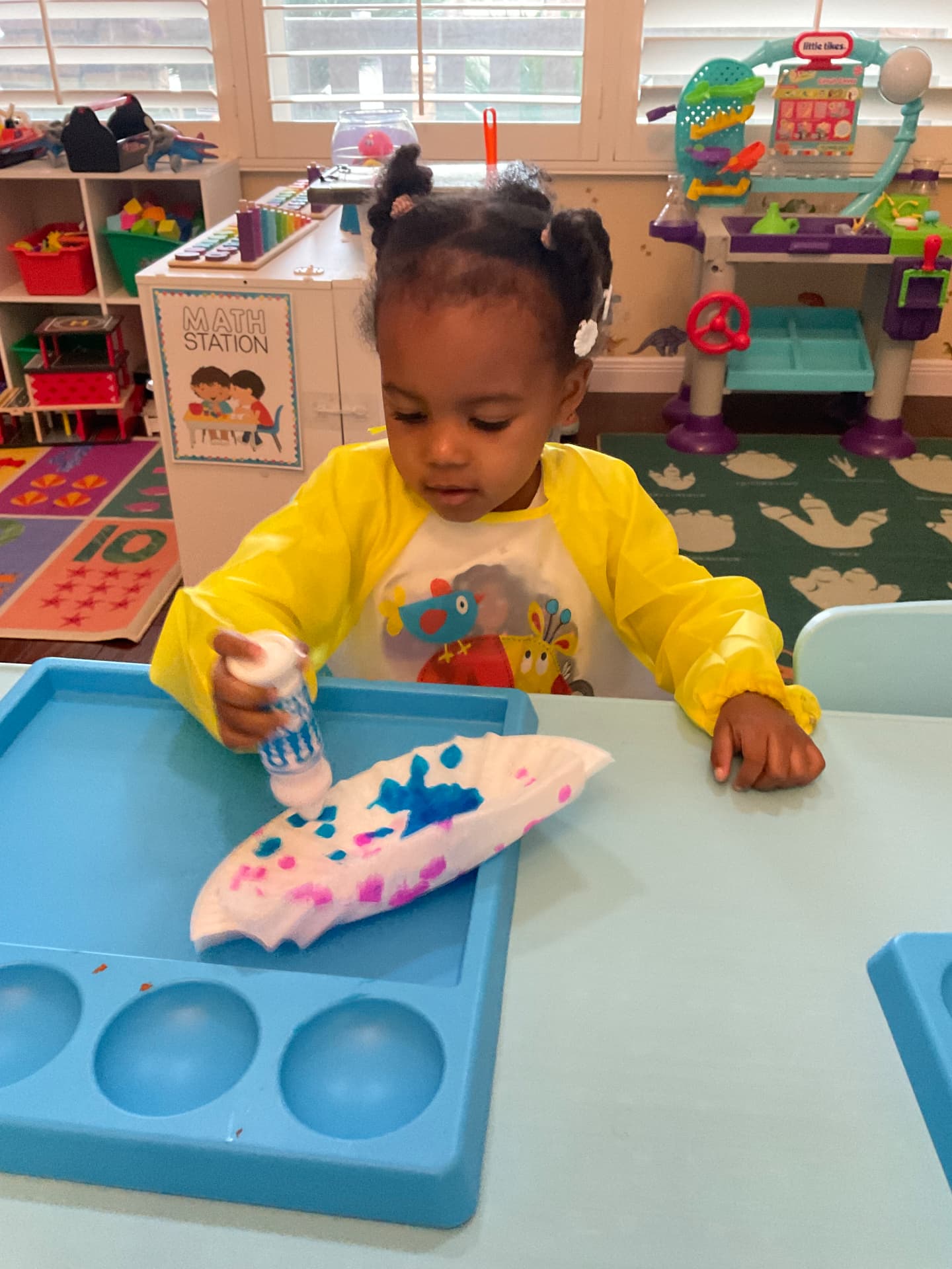 Toddler in a yellow smock dot-painting a coffee filter on a tray
