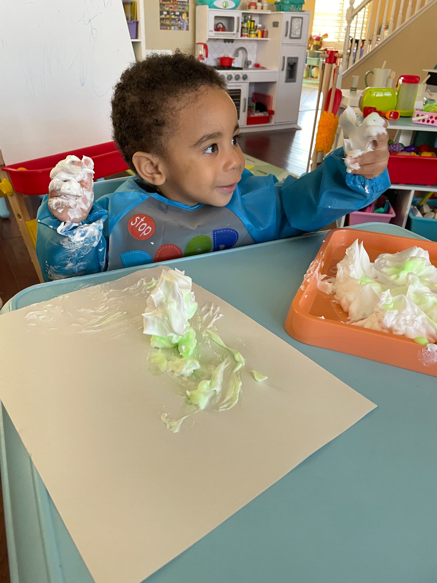 Child playing with green and white shaving cream on a tray
