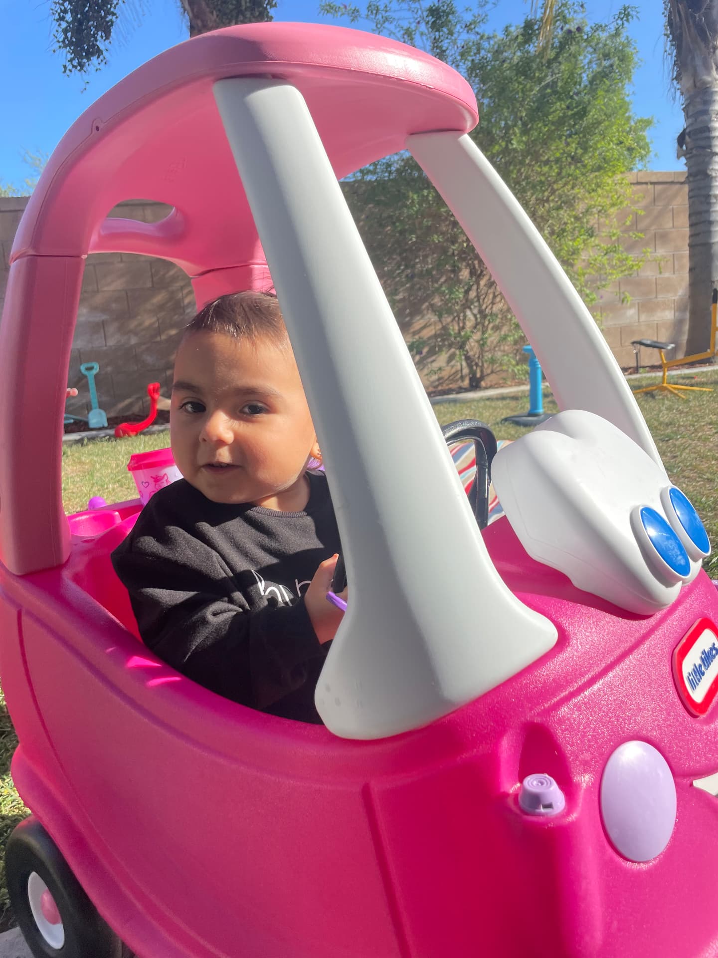 Baby sitting in a pink ride-on car in the gated backyard
