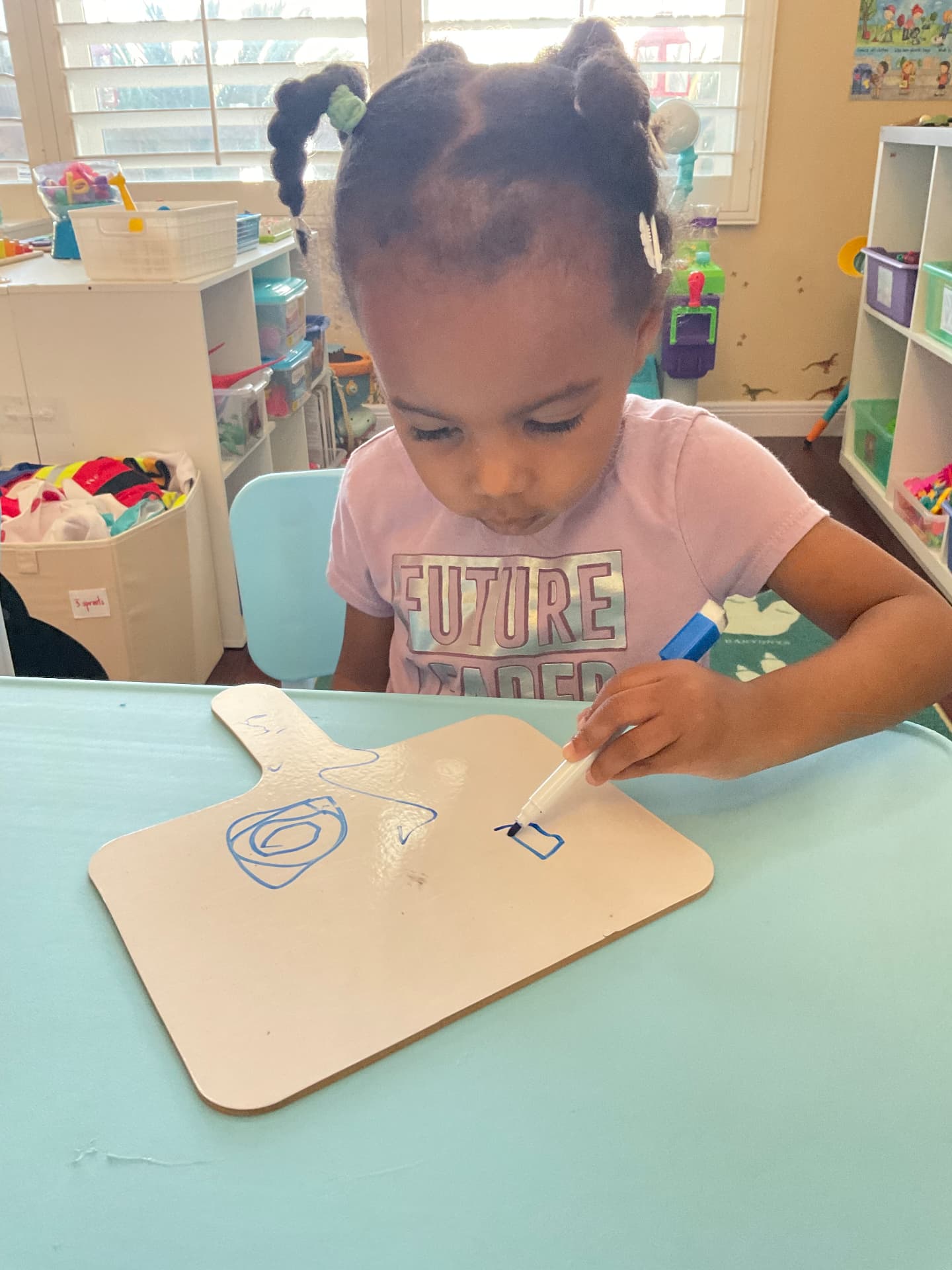 Preschooler drawing shapes with a blue marker on a small whiteboard