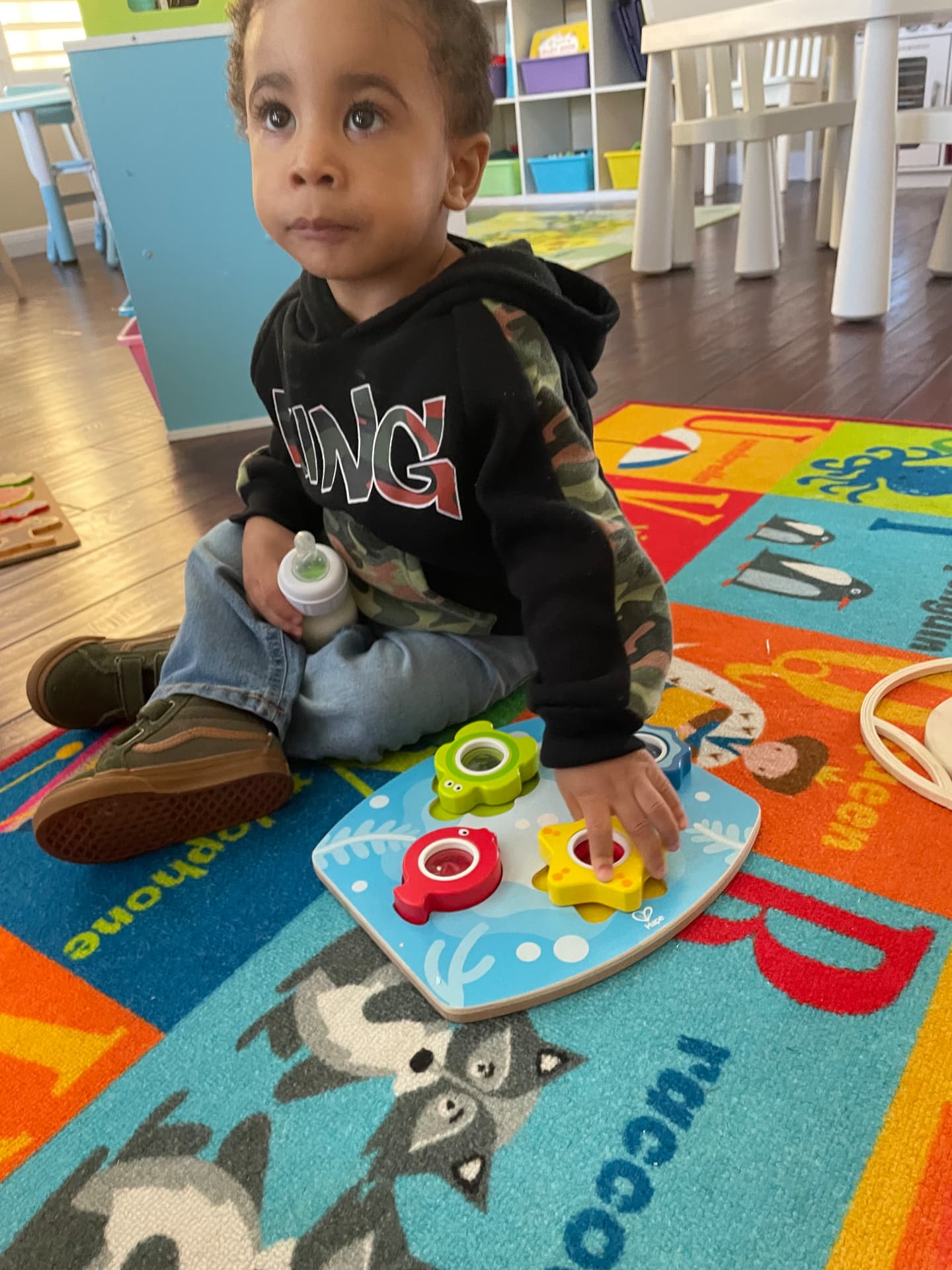Toddler fitting shapes into a wooden sea creature puzzle on the rug