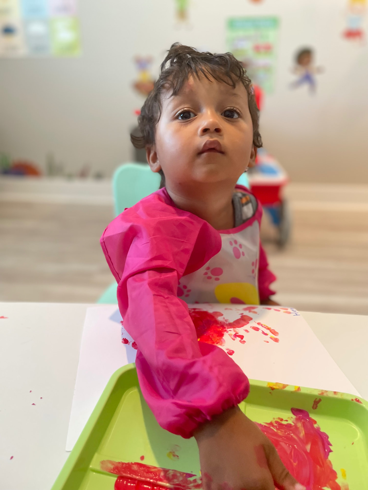 Toddler in a pink smock making handprint art with red paint