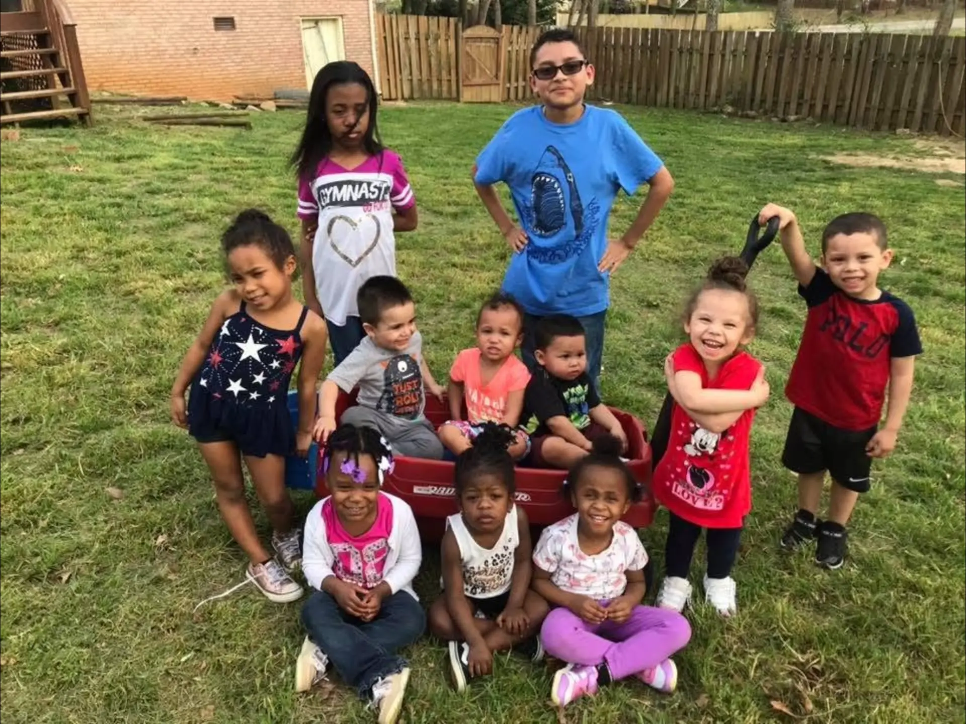 Group of children posing together with a red wagon in the backyard