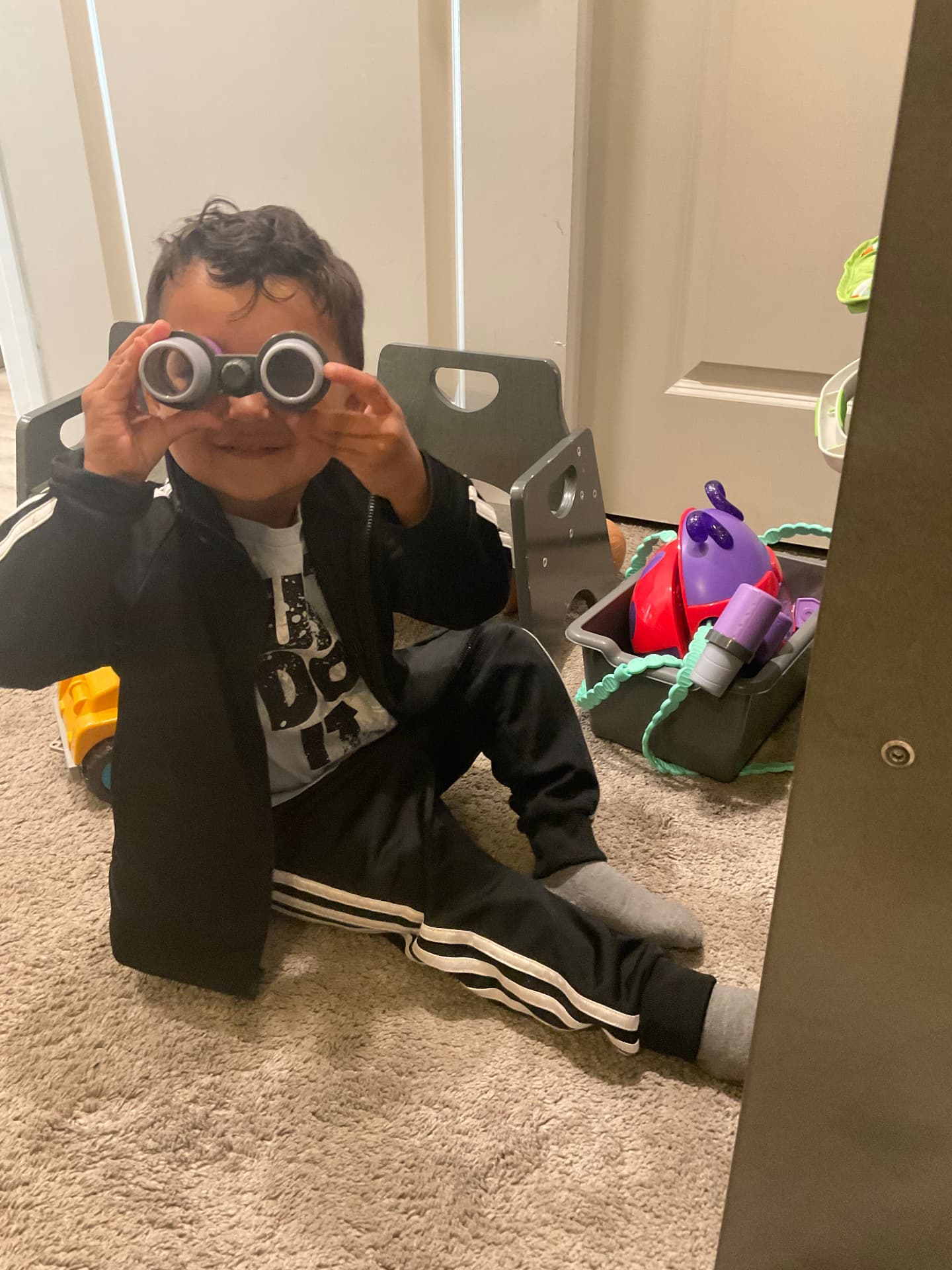 Toddler peeking through toy binoculars in the playroom