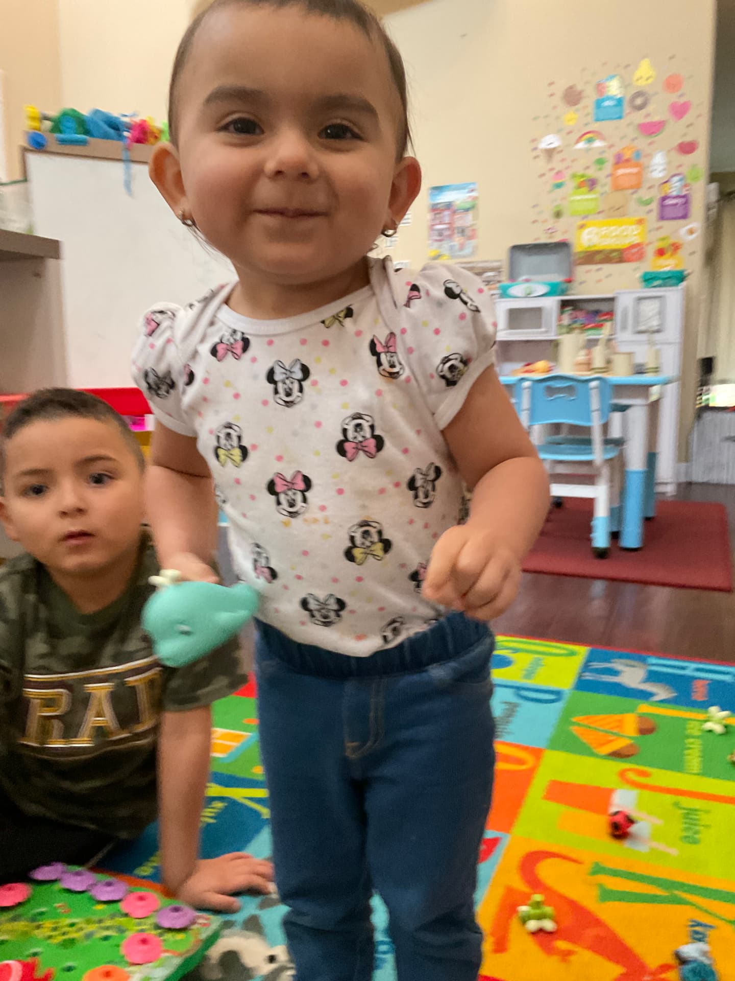 Smiling toddler standing with a toy on the alphabet rug